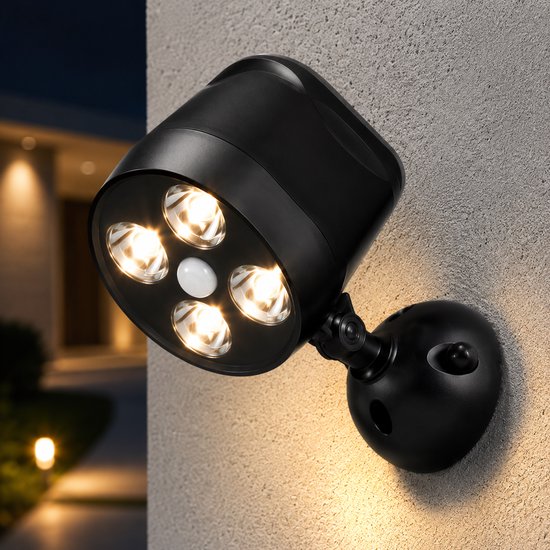 Zwarte buitenlamp met vier brandende LED's gemonteerd op een stenen muur naast een huis bij nacht.