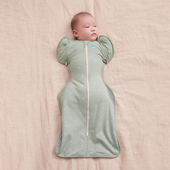 Baby in lichtgroene omslagdoek met twijgjespatroon en ritssluiting, met armen omhoog.