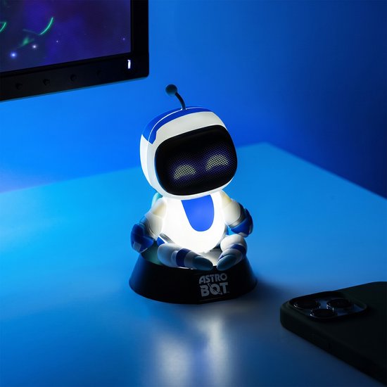 Verlichte witte en blauwe Astro Bot figuur zittend op een zwarte standaard, op een bureau.