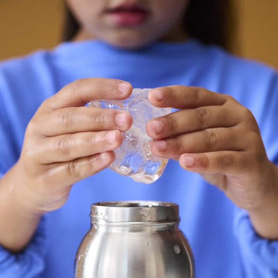 Kind houdt een grote ijsklont vast boven een zilverkleurige drinkfles.