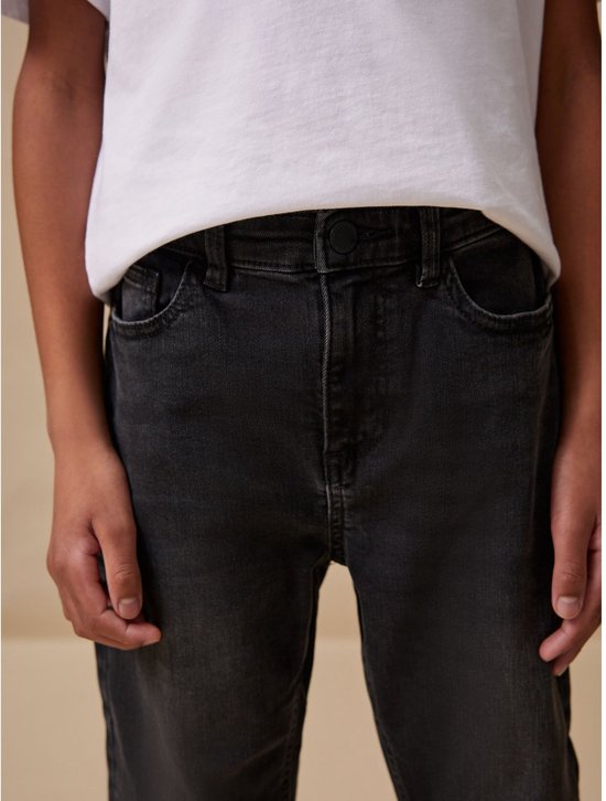 Jongen met witte T-shirt en zwarte spijkerbroek, close-up van de taille.