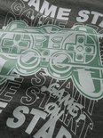 Close-up van de print op een donkergrijze sweater met een groene videogamecontroller en tekst.
