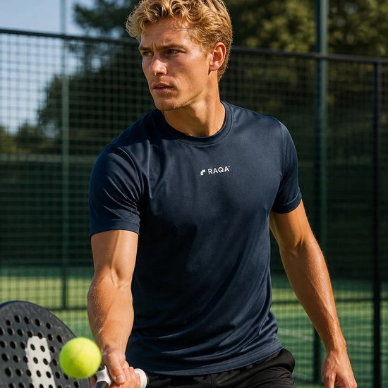 Man met een navy blauw RAQA sportshirt en zwarte broek, spelend op een tennisbaan.