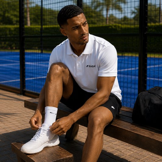 Man op een houten bankje in sportkleding, strikt witte schoenen. Draagt witte Raqa® polo.