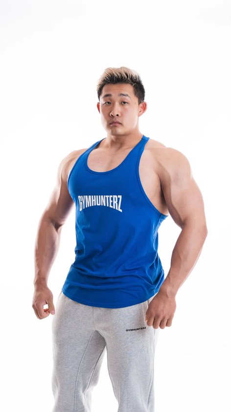 Le modèle porte un débardeur Gymhunterz bleu cobalt avec inscription blanche sur le devant et un pantalon de jogging gris.