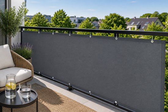 Donkergrijs balkonscherm bevestigd aan een zwarte reling, met een bijzettafel en stoel op het balkon.