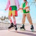 Twee kinderen met skeelers op een pad bij het strand, met palmbomen op de achtergrond.