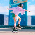 Kind met helm en skeelers, draagt een roze gestreepte blouse en kleurrijke shorts.