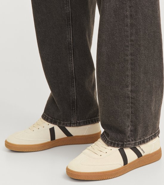 Crèmekleurige Jack & Jones sneakers met zwarte strepen, gedragen met een donkere jeans.