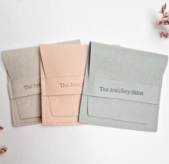 Trois pochettes à bijoux en tissu gris clair, rose et bleu sarcelle. Chaque pochette porte le logo 'The Jewellery Salon'.