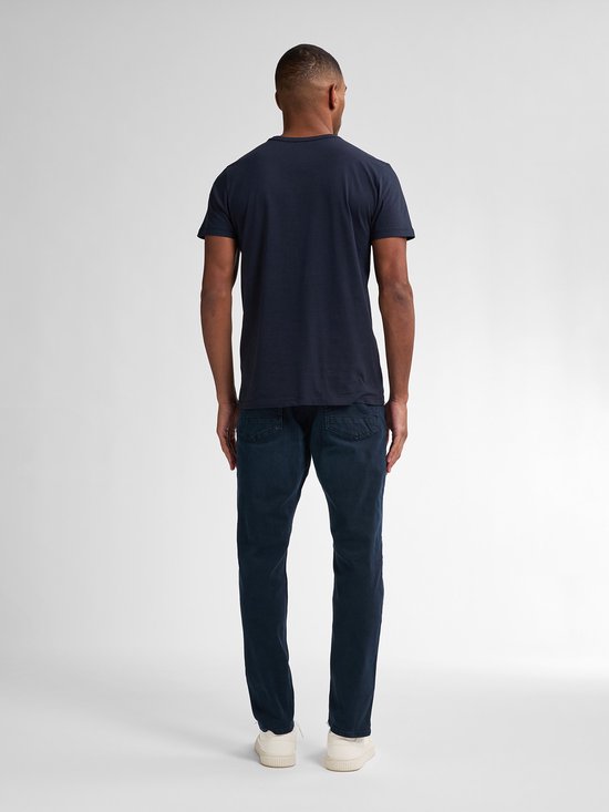 Man met donkerblauwe jeans met rechte pasvorm en donkerblauw t-shirt, van achteren gezien.