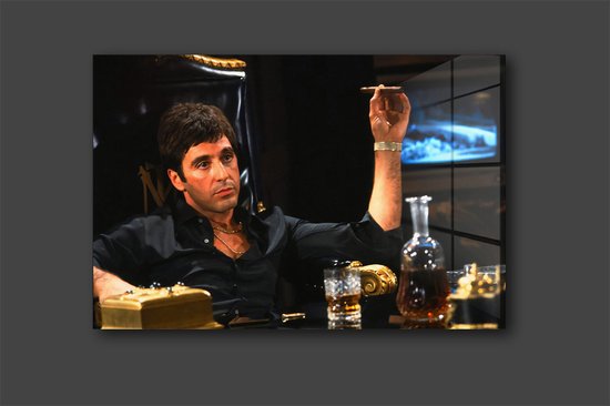 Tony Montana tenant une cigarette et un verre de whisky, assis dans un fauteuil luxueux.