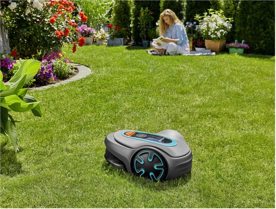 Grijze robotmaaier met turkooizen accenten op een groen gazon, vrouw leest boek op de achtergrond.