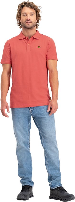 Man met steil, golvend blond haar, een rood poloshirt met korte mouwen en lichtblauwe jeans.