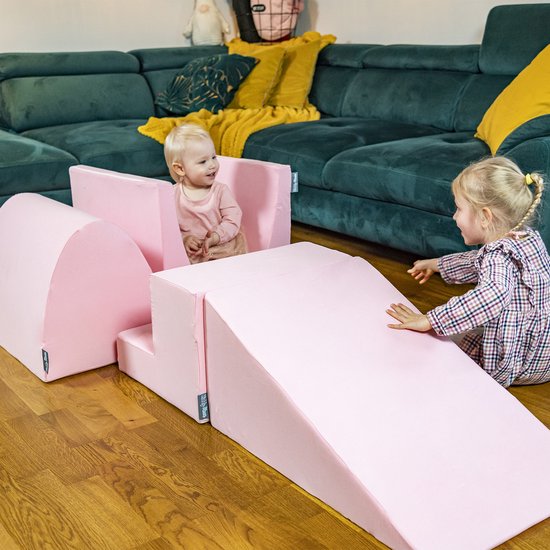 Twee kinderen spelen met roze schuimelementen, waaronder een ballenbad, hellingbaan en blokken.