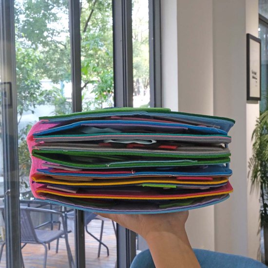 Hand die een dik, veelkleurig educatief activiteitenboek van vilt vasthoudt.