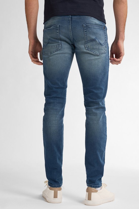 Man in een slim fit spijkerbroek, vaal blauw, met een marineblauw t-shirt. Van achteren gezien.