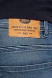 Leren label op de achterkant van een spijkerbroek met de tekst 'Petrol Industries' en 'Denim Driven Since 1989'.