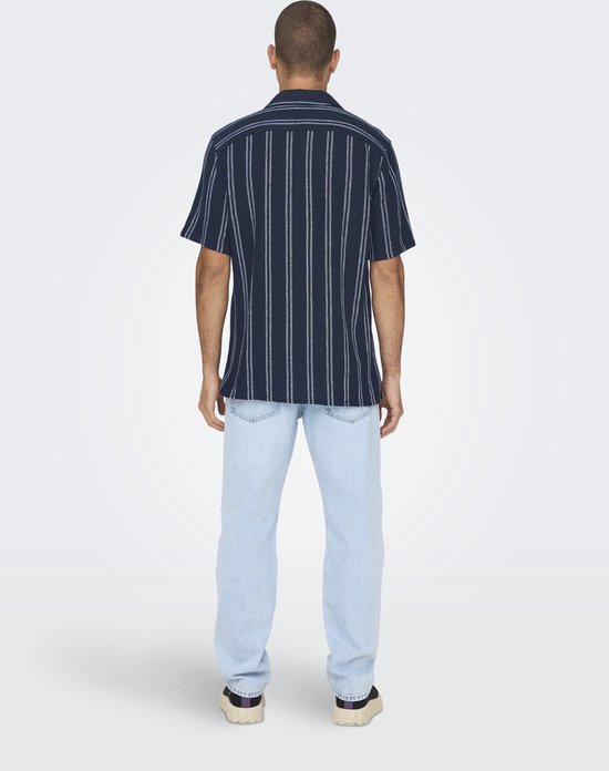 Man met de rug naar de camera, draagt een donkerblauw krijtstreeppenshirt en lichtblauwe spijkerbroek.