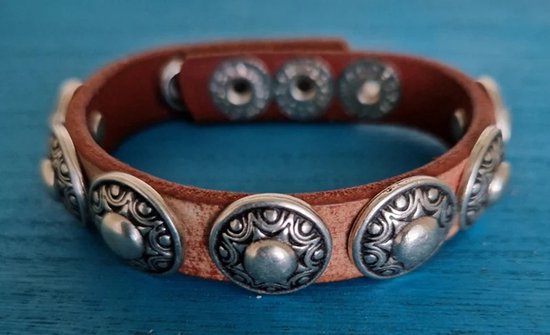 Bruine leren armband met zilverkleurige studs, op blauwe achtergrond.