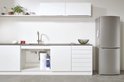Moderne keuken met chroomkraan, koelkast, witte kasten en gootsteen met filteronderdelen.