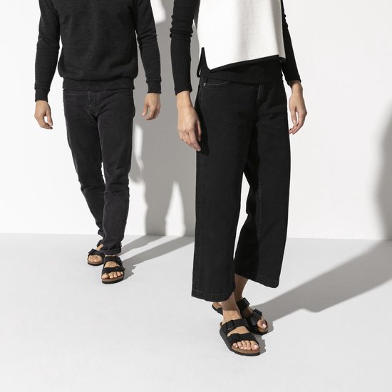 Model draagt zwarte Birkenstock Arizona slippers met jeans, een man en vrouw lopen.
