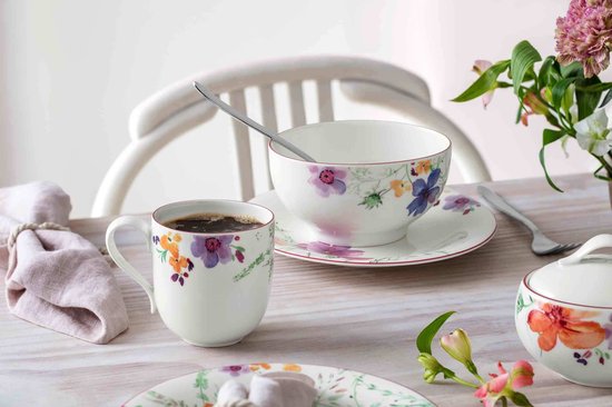 Wit koffiekopje met kleurrijke bloemenprint en rode rand. Een lepel rust in een kom met zelfde print.