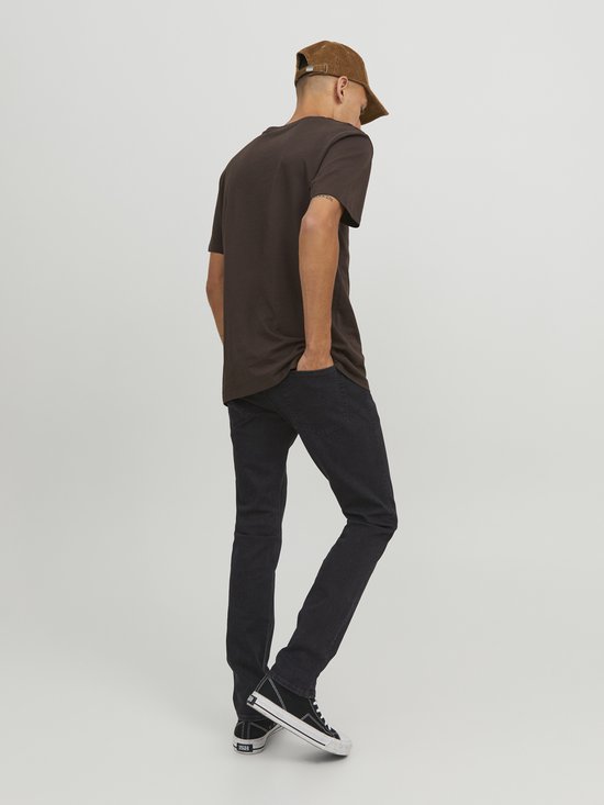 Man met bruine t-shirt, zwarte jeans, bruine pet en sneakers, van achteren gezien. Zwart denim.