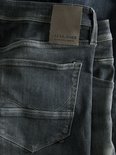 Detail van de achterkant van een donkere jeans met bruin leren merklabel.