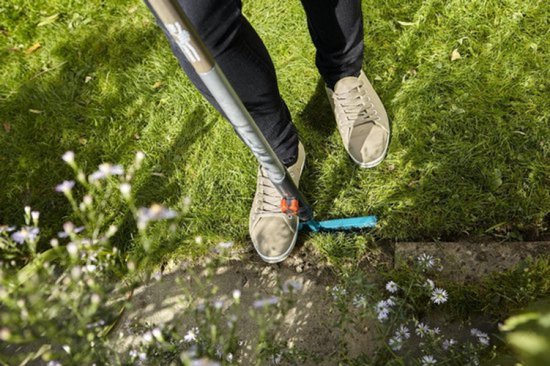 Personen gebruiken een graskantsteker, met beige sneakers en zwarte broek.