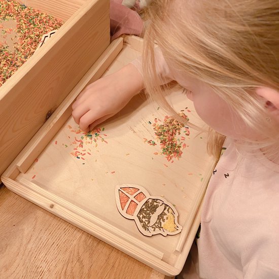 Blond jongetje met roze trui speelt met gekleurde rijst en houten Sint Nicolaas thema figuren.
