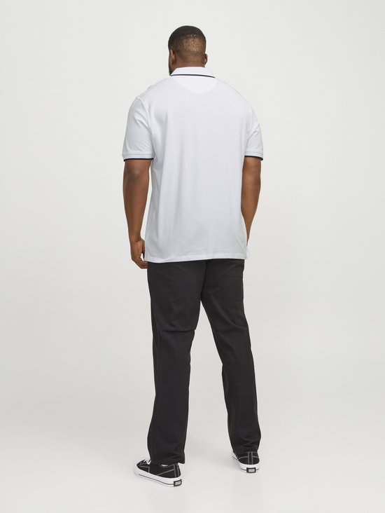 Man met baard draagt witte poloshirt met zwarte biezen en zwarte broek, achterkant zichtbaar.
