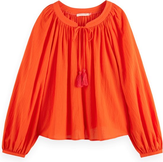 Top orange avec encolure large drapée, cordon à pompons et manches ballon.