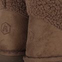 Close-up van de beige suède hiel met subtiel ingedrukt logo op donkerbruine teddy enkellaars pantoffels.