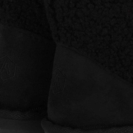 Close-up van de beige suède hiel met subtiel ingedrukt logo op zwarte teddy enkellaars pantoffels.