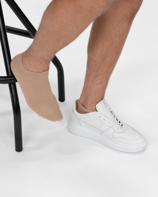 Zittende persoon met beige enkelsok en witte sneaker.