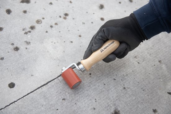Grijze handschoen gebruikt om een rode aandrukroller met houten handvat over een naad te rollen.