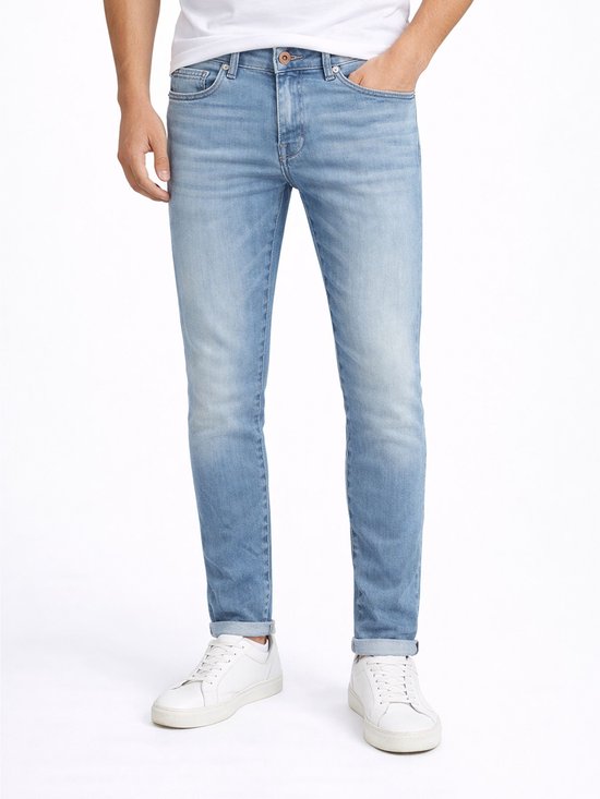 Lichtblauwe spijkerbroek, slank gesneden, met een stonewashed look. Een man draagt de broek met een wit T-shirt en witte sneakers.