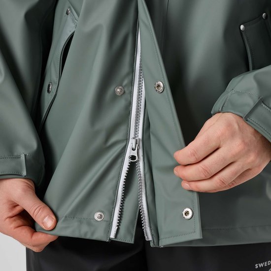 Gedetailleerde opname van de ritssluiting van een groene jas die een man sluit.