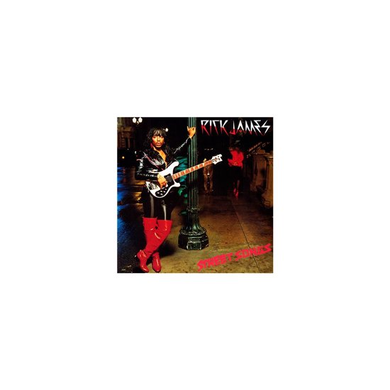 Rick James met basgitaar, staand bij een lantaarnpaal, met rode laarzen.