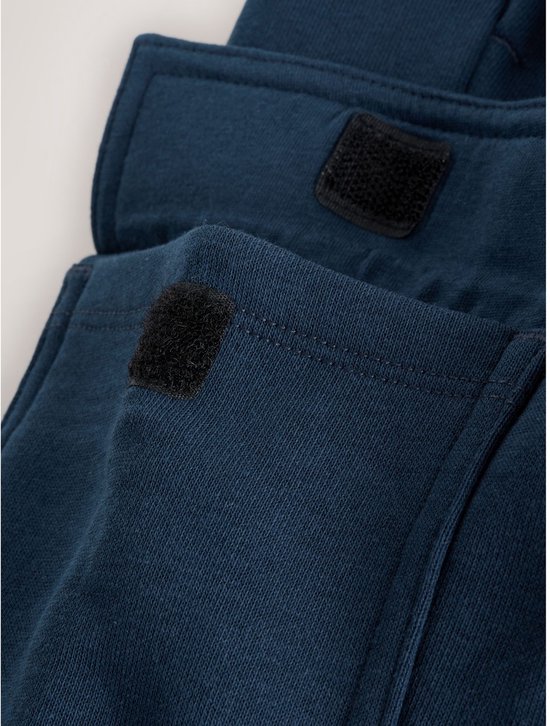 Close-up van de klittenbandsluitingen op de cargo zakken van een marineblauwe joggingbroek.