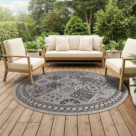Rond vloerkleed met mozaïekpatroon op een houten terras, met tuinmeubilair.