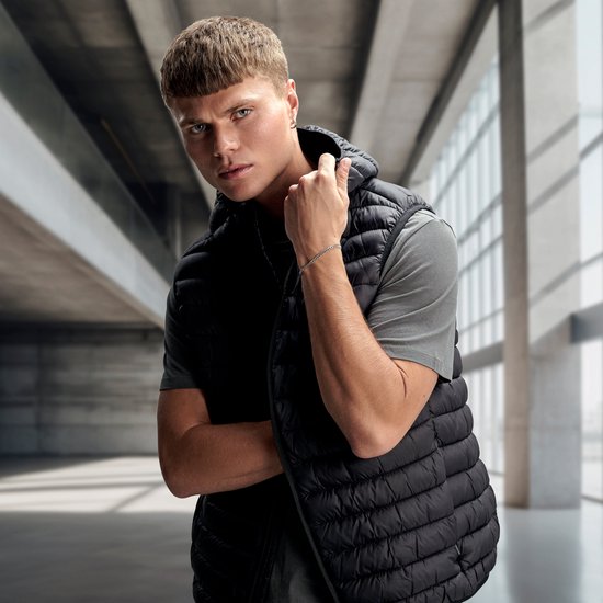 Jeune homme aux cheveux bruns courts, portant un gilet noir et un t-shirt gris. Bracelet argenté visible.