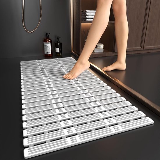 Voet op een lange, grijze antislip badmat op een donkere vloer.