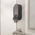 Zwart Aqara slim deurslot met cirkelvormig handvat, gemonteerd op een witte deur naast een zilveren deurklink.