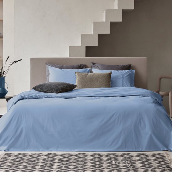Housse de couette bleue avec taies d'oreiller assorties sur un lit avec têtes de lit grises.