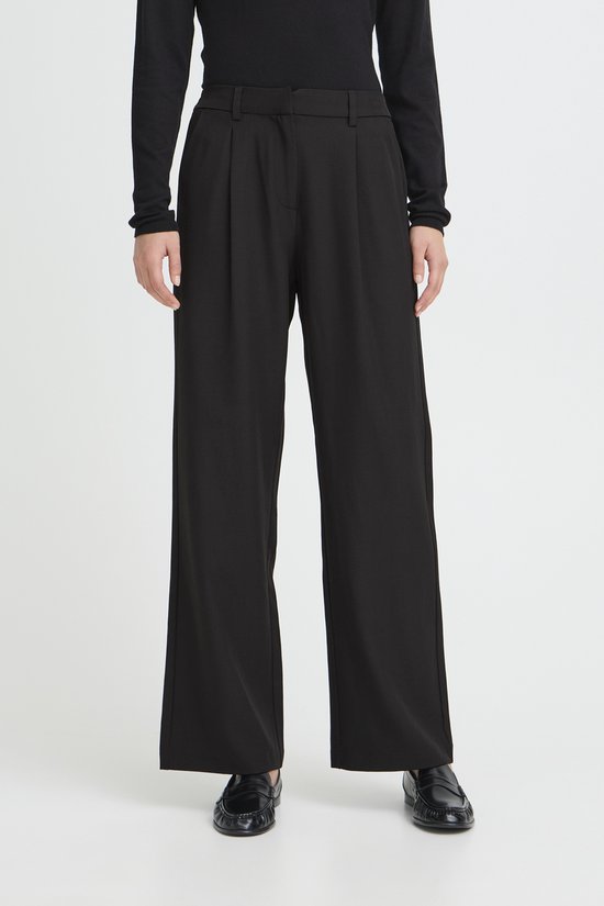 Vrouw in zwarte wijde broek met plooien aan de voorkant, deels van voren gezien.