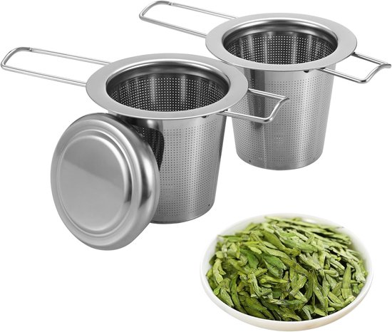 Twee zilverkleurige thee-eieren, één met deksel, en een kom met groene theebladeren.