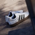 Twee witte sneakers met zwarte Adidas strepen en bruine zool, gefotografeerd op straat.