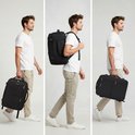 Man met witte t-shirt, beige broek en witte sneakers, draagt de zwarte reistas in de hand, op de rug en in de hand.